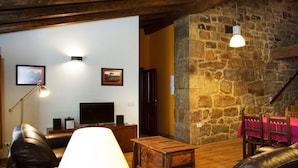 A cozy living room with a stone wall, leather sofas, a wooden coffee table, a TV, and a lamp. - La Casa del Vino (Fermoselle)