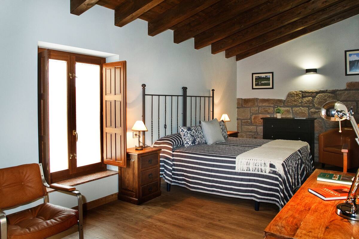 Ein Schlafzimmer mit Bett, Nachttischen, einem Sessel, einem Schreibtisch und einem Steinkamin.