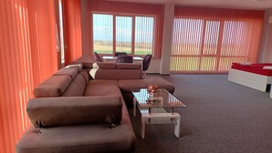 A modern living room with a sectional sofa, a glass coffee table, and a white bed. - Ubis hotel (Rodopi)
