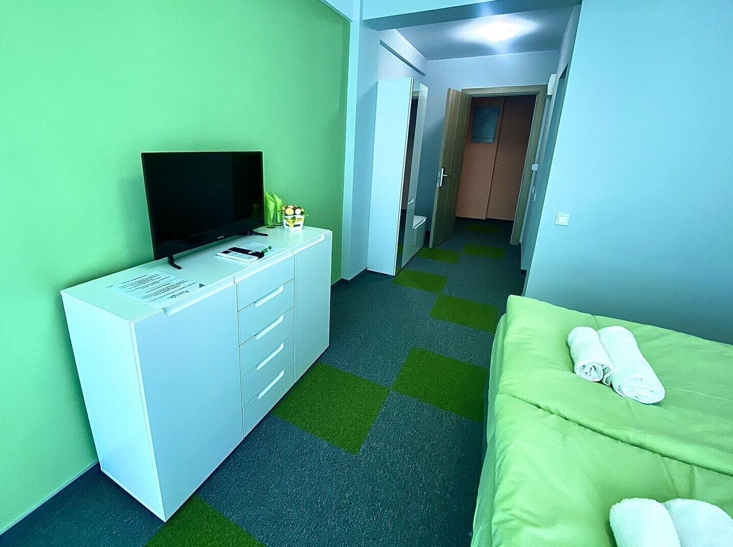 Ein Hotelzimmer mit weißem Schreibtisch, einem Flachbildfernseher, einem grünen Sofa und einem grünen Teppich.