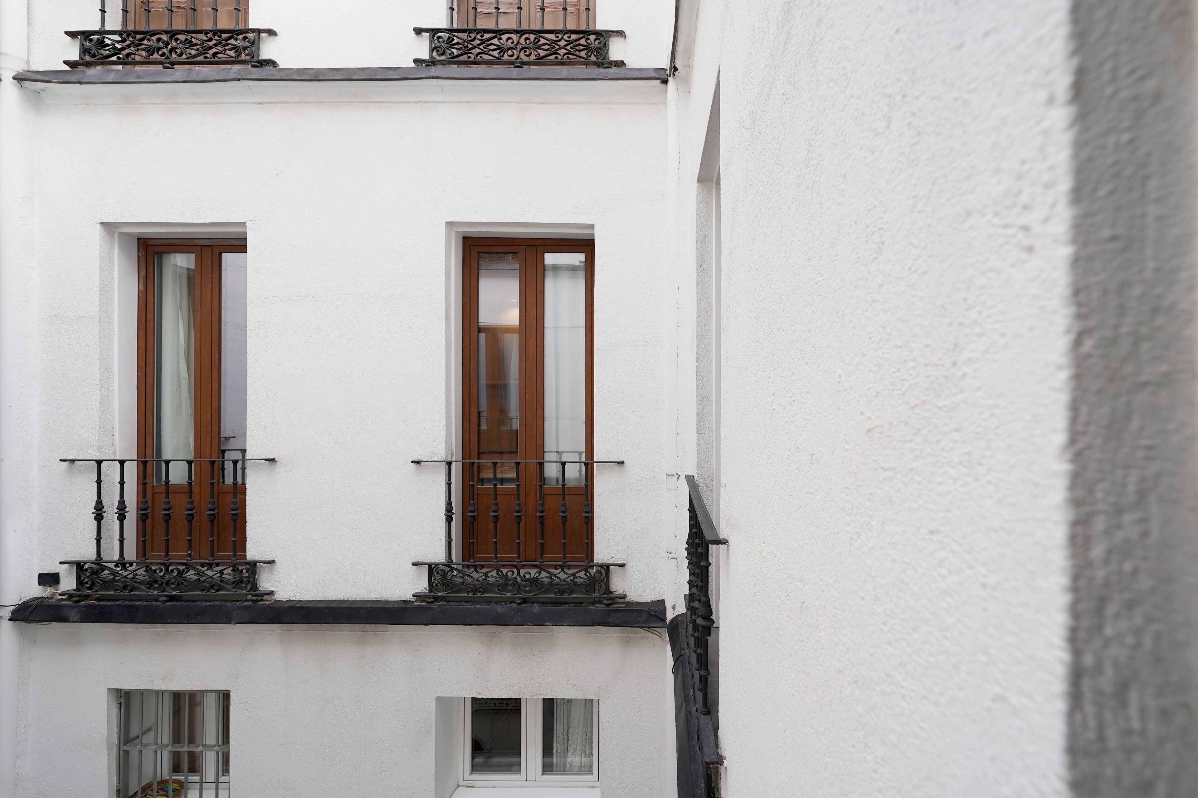 A white building with two windows on the ground floor and two balconies with wrought iron railings.