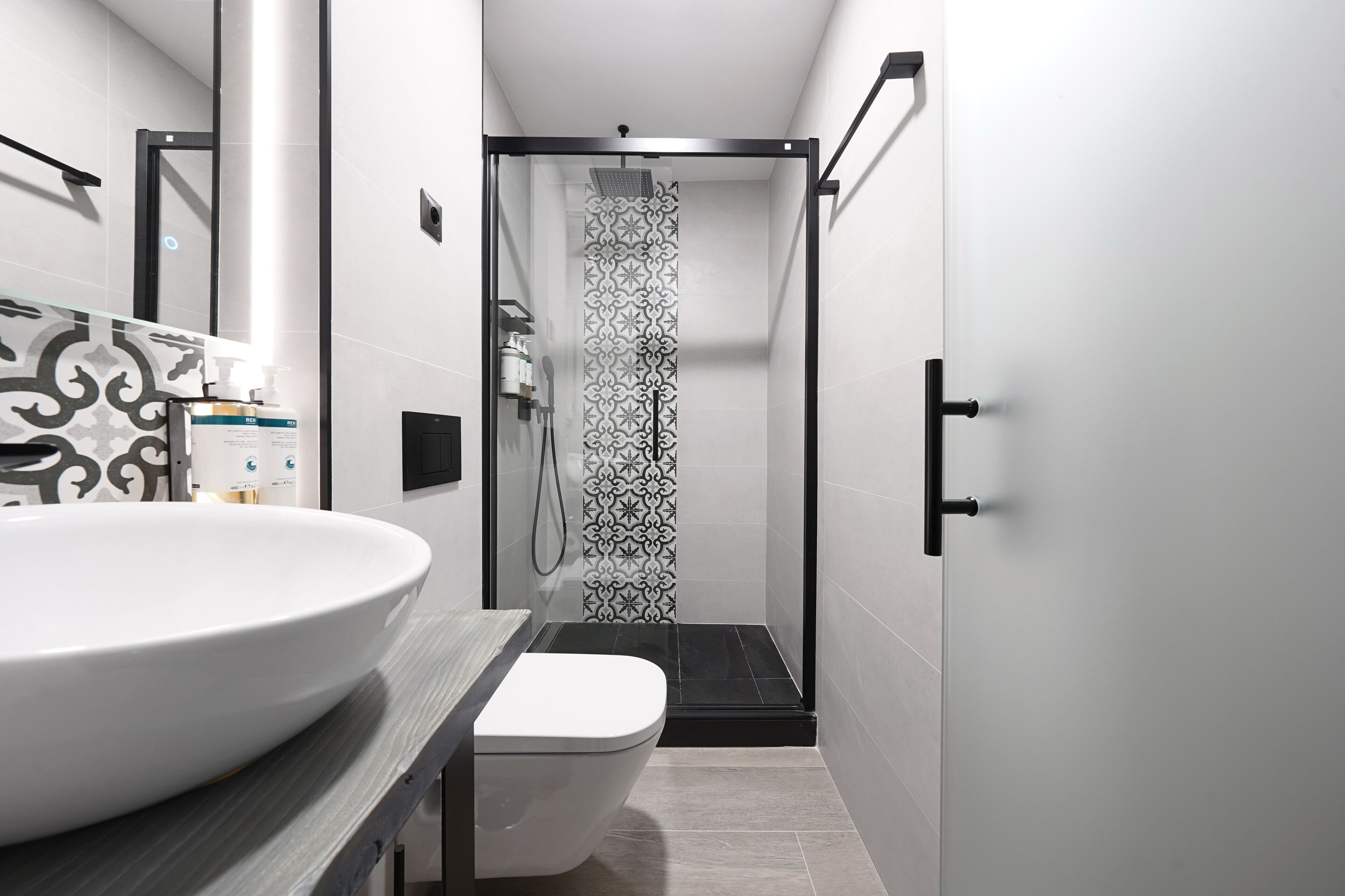 A modern bathroom with a large white sink, a toilet, and a shower area with a patterned glass door.