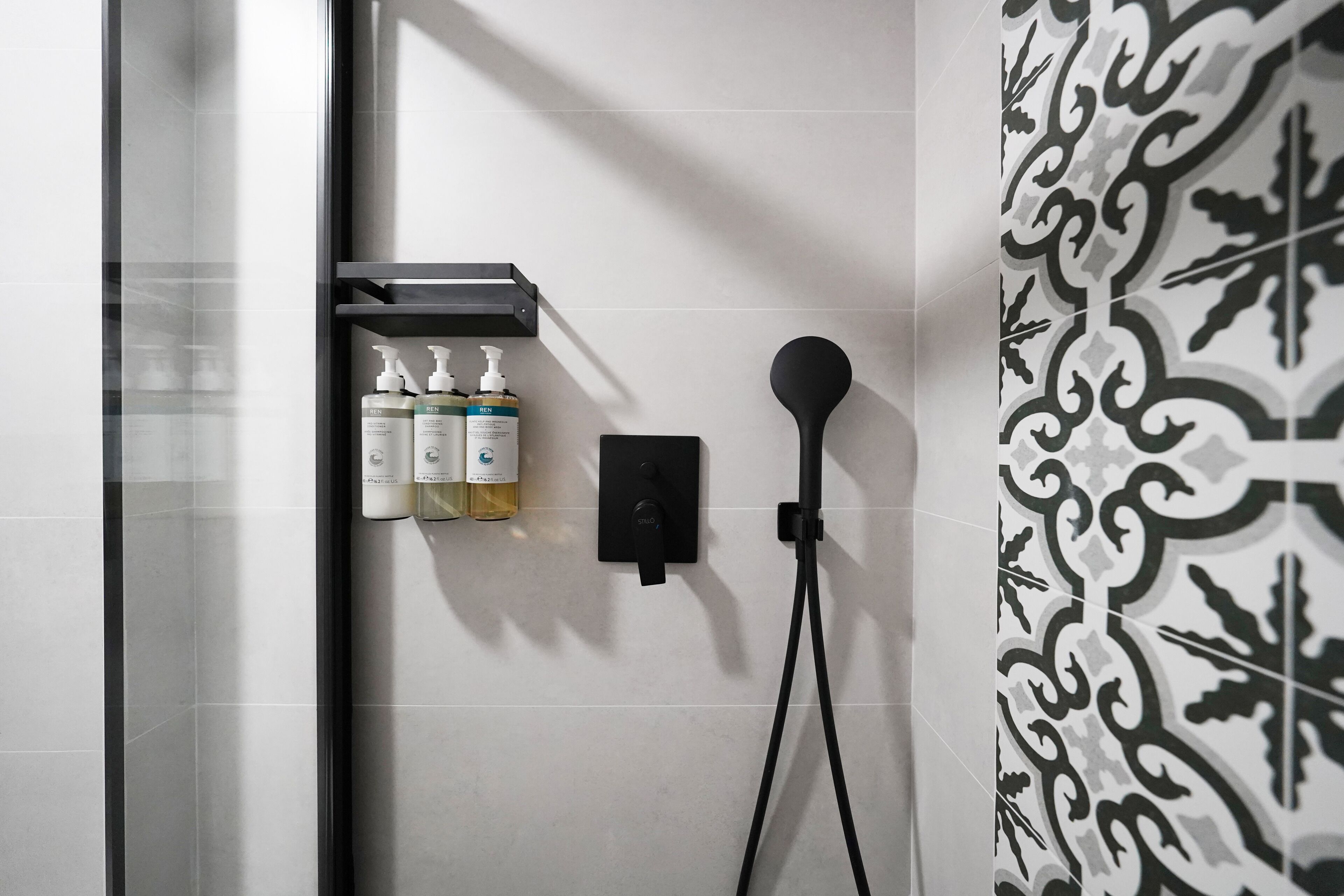 A bathroom with a shower, a wall-mounted soap dispenser, and a towel rack.