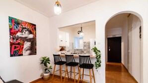 Une cuisine moderne avec des tabourets de bar, une plante en pot et une œuvre d’art colorée accrochée au mur.