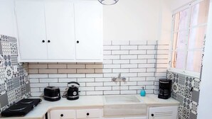 Une cuisine de taille réduite avec des meubles blancs, un pare-feu en carrelage et un évier. On y trouve deux bouilloires et une machine à café sur le plan de travail.
