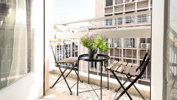 Un balcon agrémenté d’un pot de fleurs, de deux chaises en bois et d’une petite table ronde.