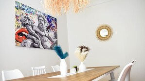 A dining area with a wooden table, white chairs, a modern chandelier, a colorful abstract painting, and a round mirror on the wall. - Acropolis Rooftop Monastiraki. (Athina)
