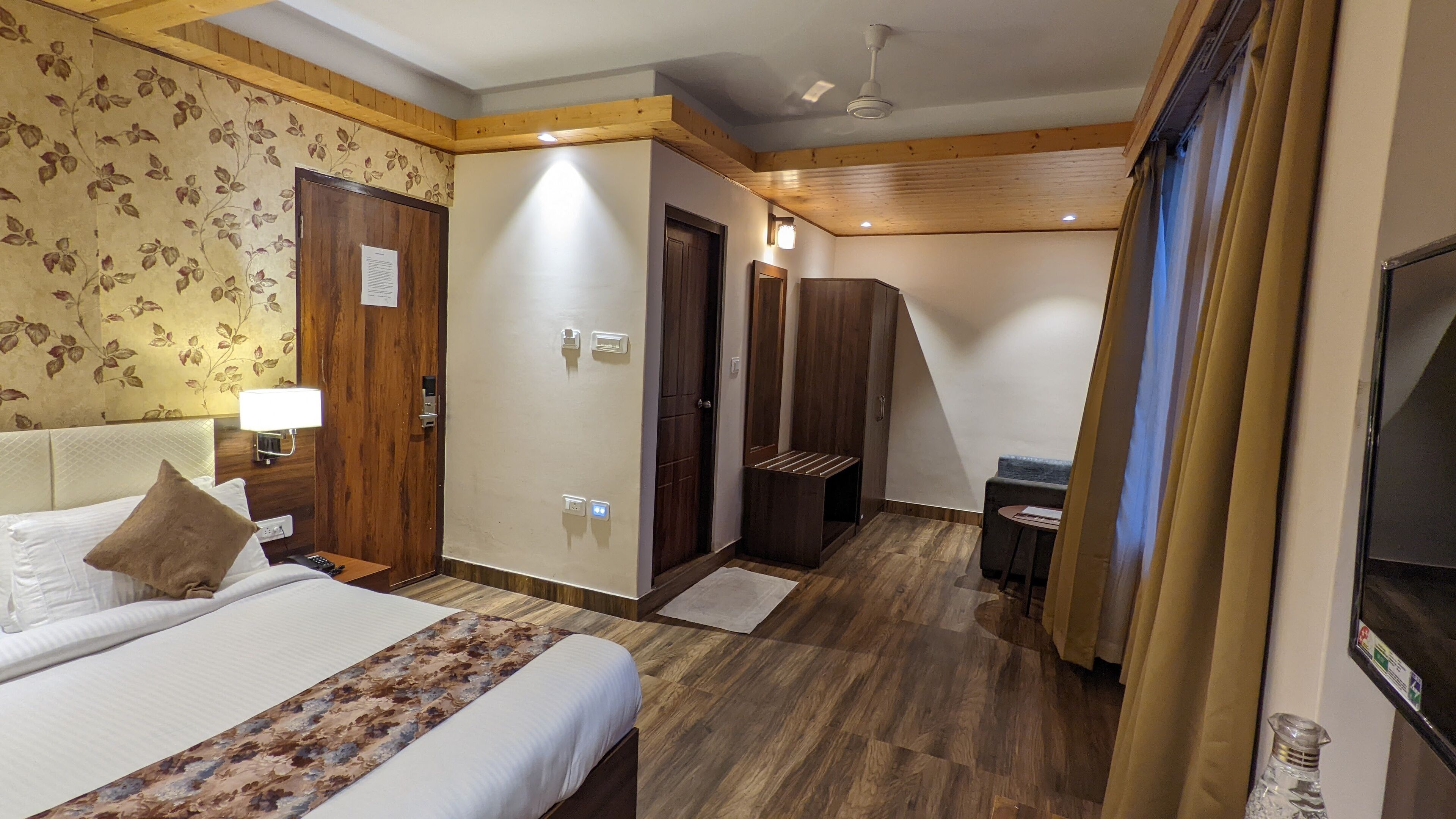 A hotel room with a bed, a desk, a chair, a mirror, and a television.