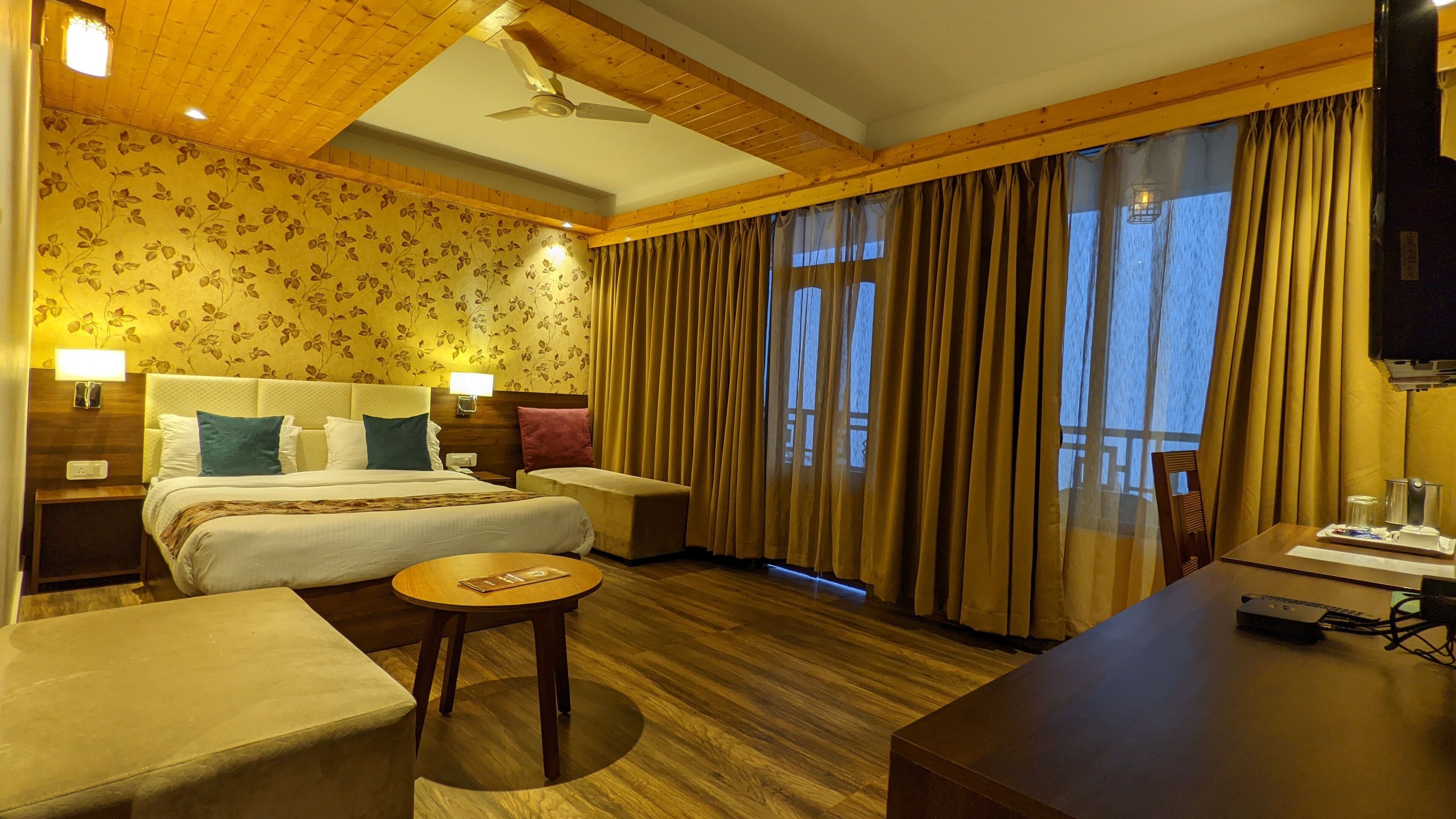 Habitación de hotel con cama, mesitas de noche, escritorio, silla, mesa redonda y televisor.