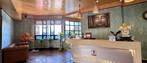 A reception area with a wooden ceiling, a reception desk, a Buddha statue, and a large window with a view.