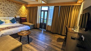 Ein Hotelzimmer mit einem großen Bett, einem Schreibtisch mit Fernseher, einem kleinen Tisch und einem Balkon mit Vorhängen.