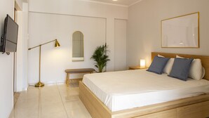 A modern bedroom with a large bed, bedside tables, a floor lamp, a mirror, and a television on the wall. - Dls*apartment (Αθήνα)