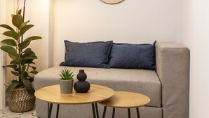 A modern living room with a sofa, two round tables, a potted plant, a floor lamp, and a wall-mounted mirror. - Dls*apartment (Αθήνα)