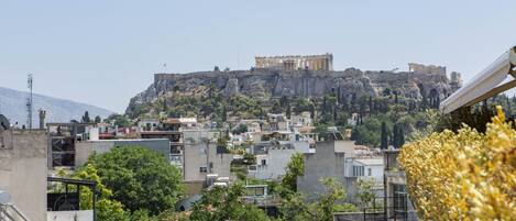 A view of a cityscape with a prominent ancient ruin on a hill, modern buildings, and a rooftop with a colorful mural.
