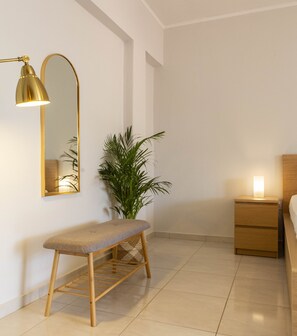 Une chambre à coucher au style minimaliste, avec un banc en bois, une table de chevet avec une lampe, un grand miroir et une plante en pot.
