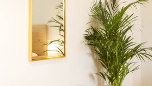 A bench with a cushioned seat and wooden legs, a gold-framed mirror, and a tall green plant beside it. - Dls*apartment (Αθήνα)
