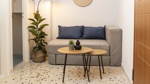 A compact living space with a grey sofa, a round mirror, a hanging light fixture, and a small table with a potted plant. - Dls*apartment (Αθήνα)