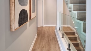 A hallway with wooden flooring, a glass railing staircase, and framed artwork on the walls. - Pearl Valley Golf Lodge - Loadshedding f (Paarl)