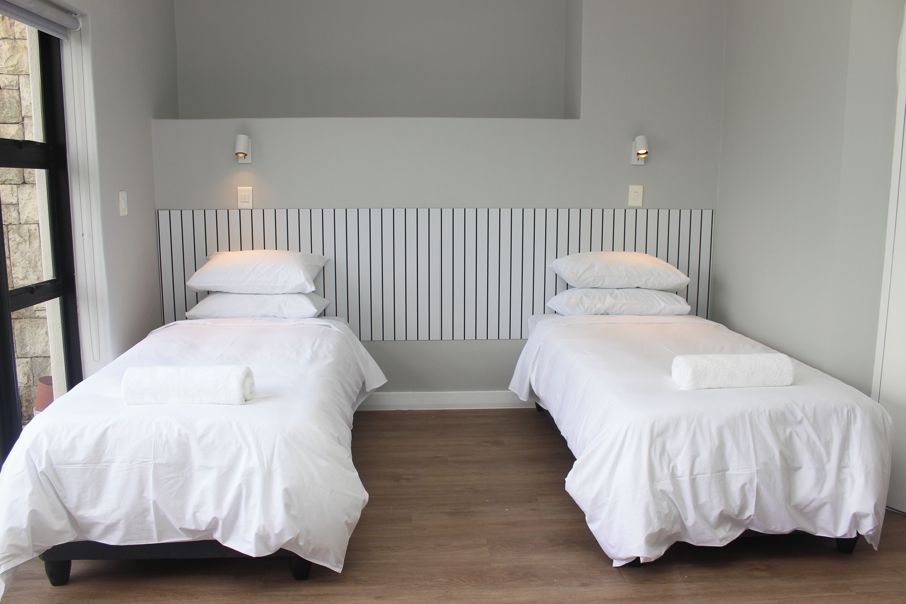 Une chambre d’hôtel avec deux lits, une tête de lit à rayures et des lampes de chevet.