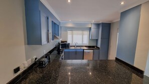A kitchen with blue cabinets, a black countertop, a window, and a built-in microwave. - Pearl Valley Golf Lodge - Loadshedding f (Paarl)