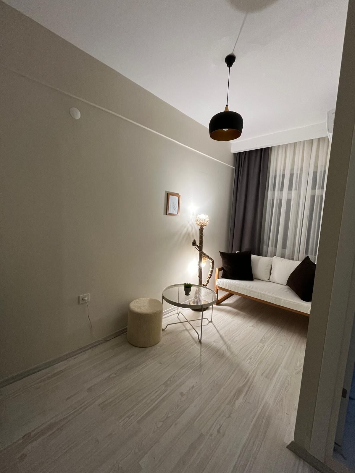 A modern living room with a sofa, a round glass coffee table, a lamp, and a ceiling light.