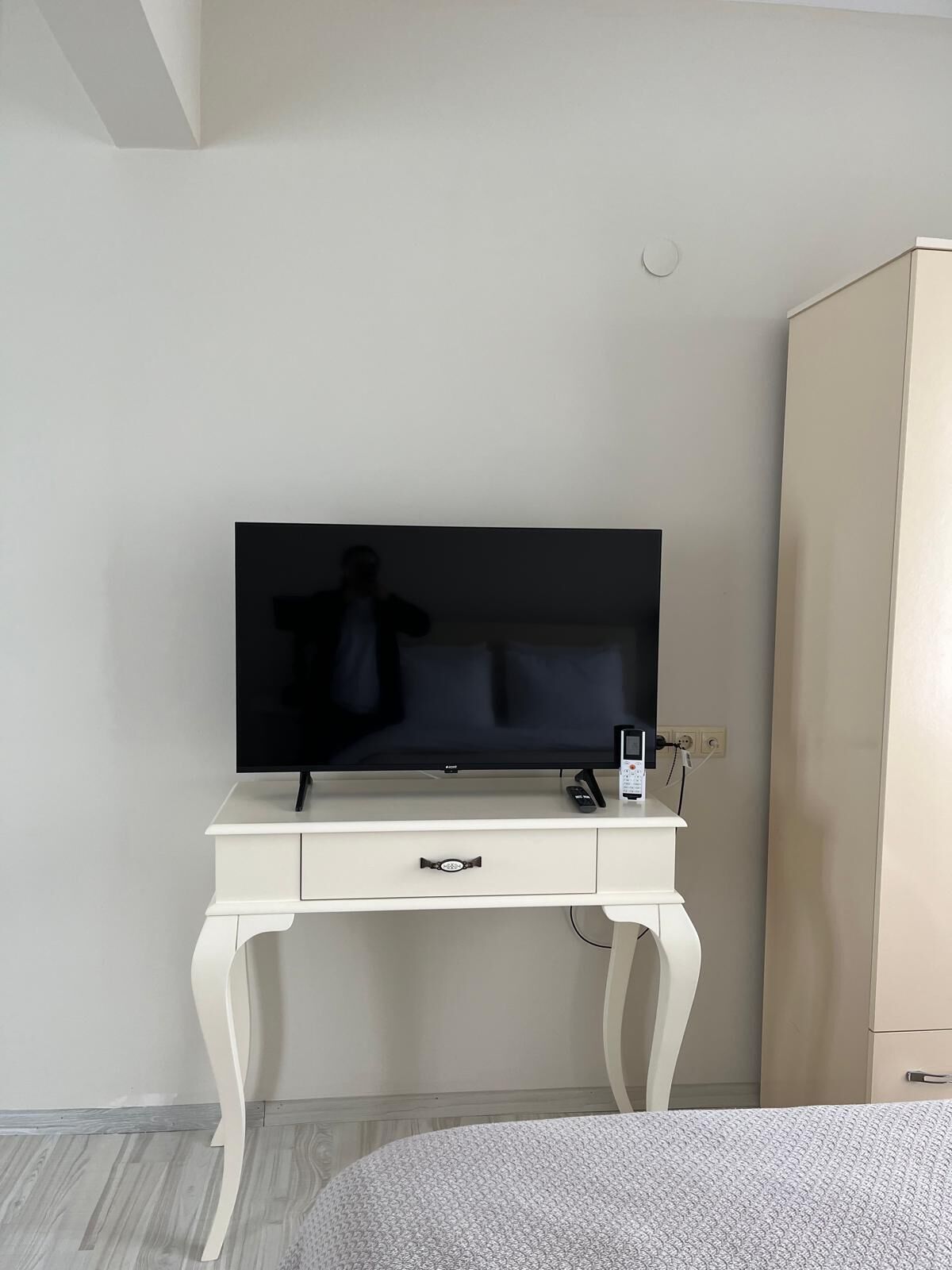Une chambre moderne avec un téléviseur à écran plat posé sur une console blanche, une table de chevet avec une lampe et une armoire.