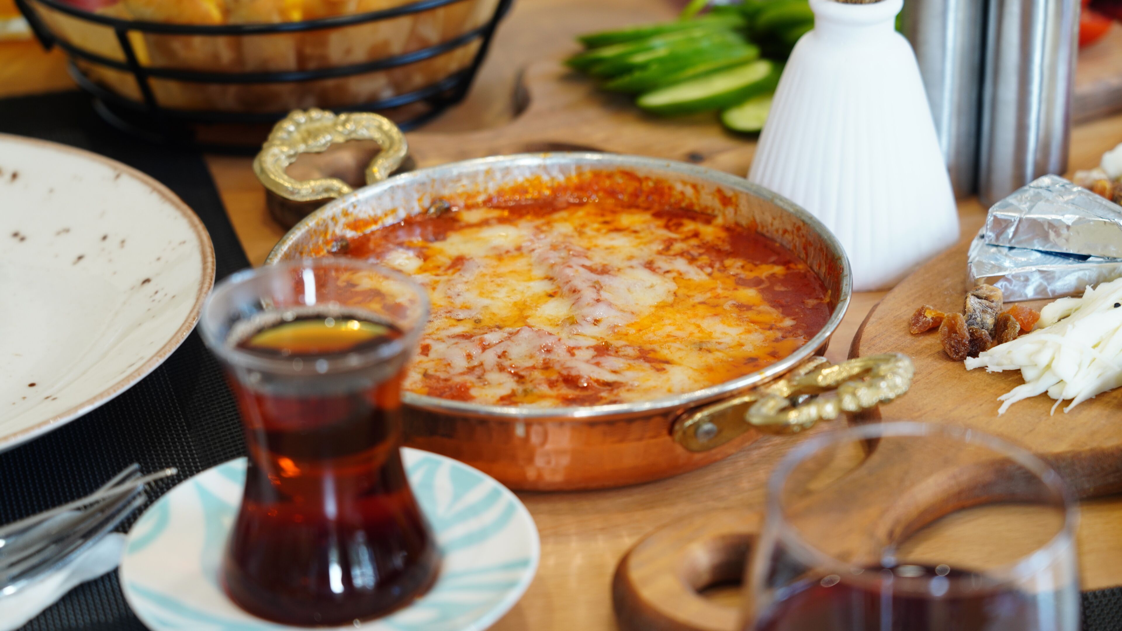 A meal with a dish in the center, a glass of tea, and various food items on the table.