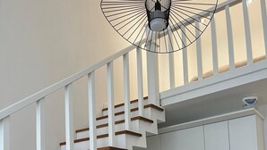 A modern kitchen with white cabinets, a wooden staircase, and a TV on a wooden stand. - Mehmetbey Çaka (Persembe)