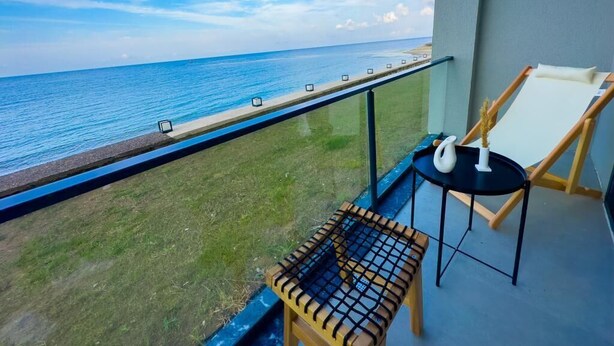 A balcony with a view of the ocean, a small table, a chair, and a whiteboard. - Mehmetbey Çaka (Persembe)