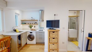 A compact kitchen with a washing machine, a flat-screen TV, and a small dining area. - The Conifer Studio | Oxford Holiday Let | 1 Bed & Sleeps 1 (Oxford)