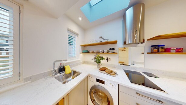 A compact kitchen with a built-in washing machine, a window with blinds, and a skylight. - The Conifer Studio | Oxford Holiday Let | 1 Bed & Sleeps 1 (Oxford)