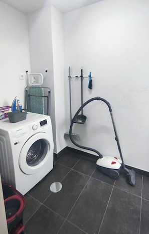 A laundry area with a washing machine, a vacuum cleaner, and a drying rack.