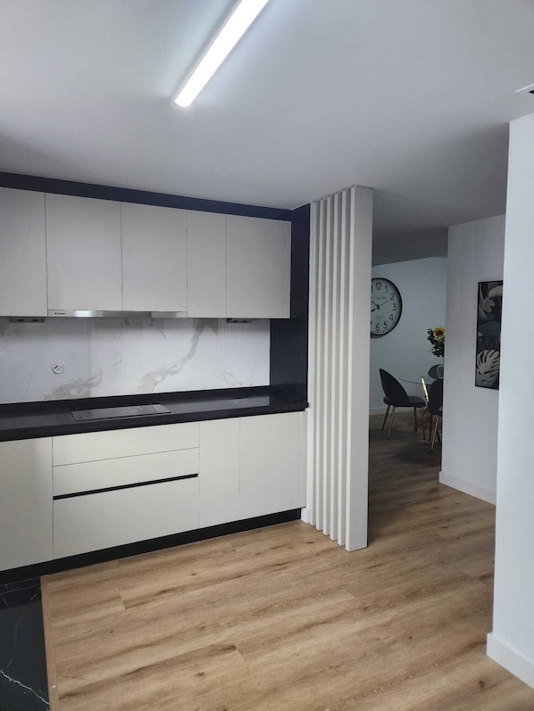 A modern kitchen with white cabinets, a black countertop, and a wooden floor.