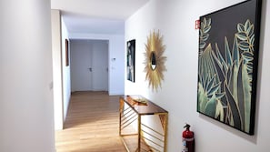 A hallway with a wooden floor, a glass-top table, and two framed artworks on the walls.