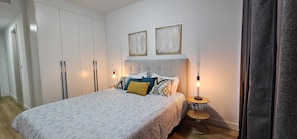 A bedroom with a bed, a bedside table with a lamp, a wardrobe, and two framed pictures on the wall.