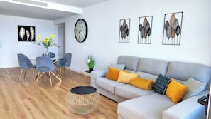 A modern living room with a grey sofa, a dining table with chairs, a round coffee table, and wall art.