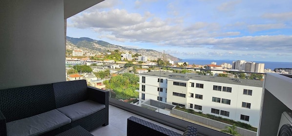 A balcony with a view of a cityscape, including buildings and mountains.