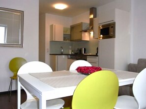 Une cuisine compacte dotée d’appareils électroménagers modernes, une table à manger avec des chaises et un petit coin salon.