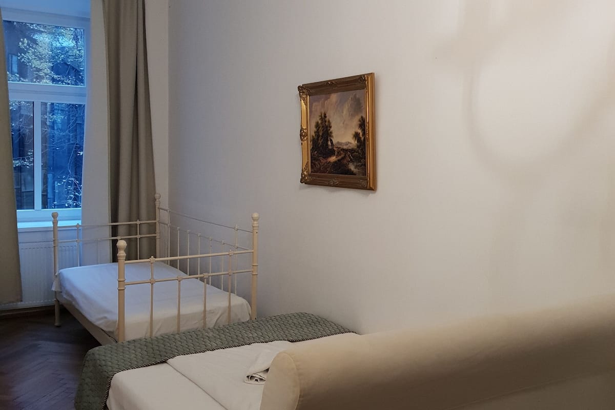 A bedroom with two beds, a window with curtains, a painting on the wall, and a chandelier.