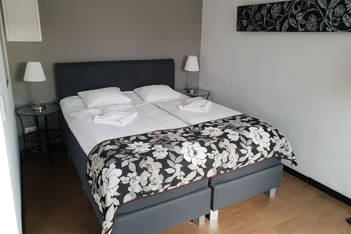 A neatly made bed with white linens and a floral-patterned bedspread, flanked by two bedside lamps on a round table beside the bed.