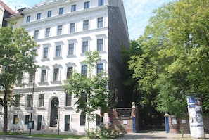 Ein historisches Gebäude mit einer klassischen Fassade, einem modernen Anbau und einem kleinen Garten.