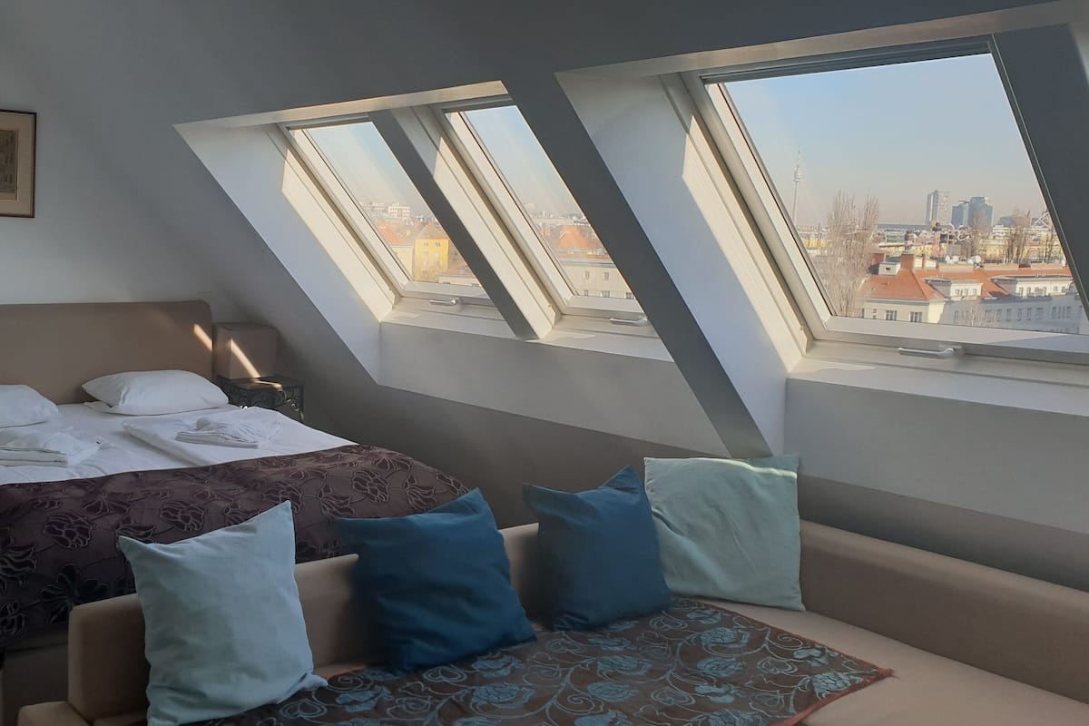 A bedroom with a bed, a nightstand, a chair, and a window with a city view.