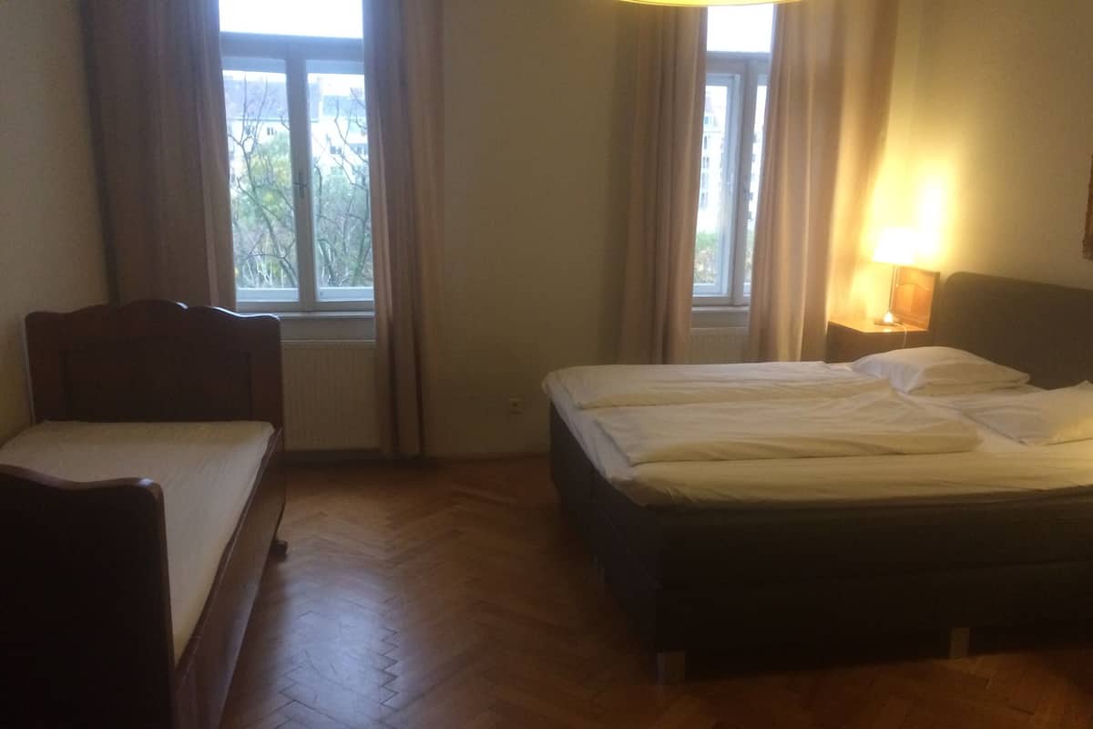 A room with a wooden floor, a single bed, a small bedside table with a lamp, and a window with curtains.