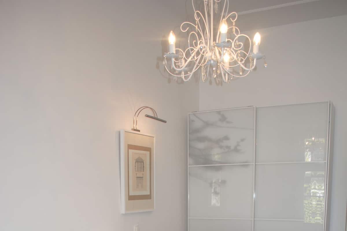 A bedroom with a large bed, a chandelier, a framed picture, and a wardrobe.