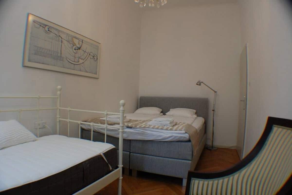 A bedroom with two beds, a desk, and a chair. There is a painting on the wall and a lamp on the desk.