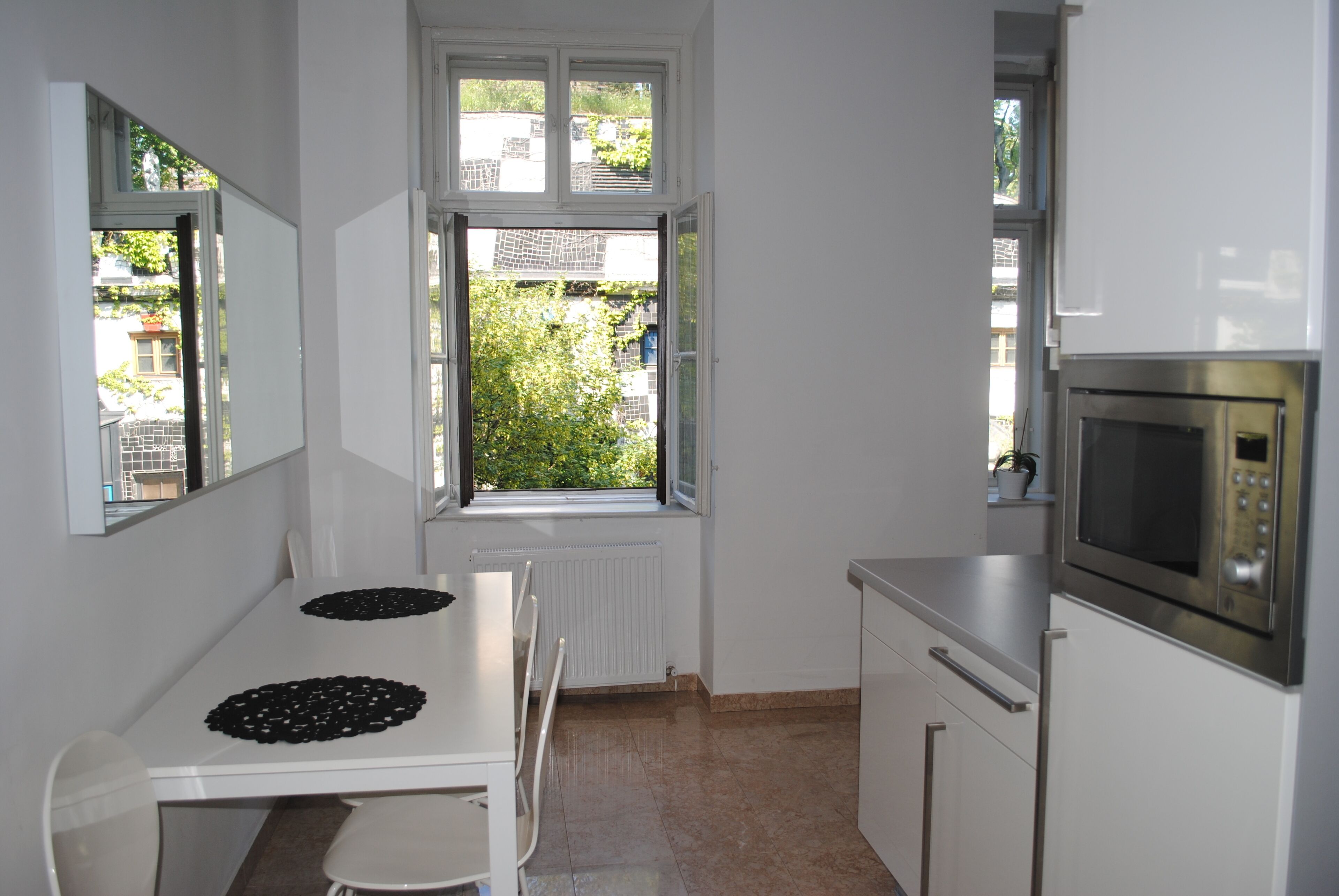 Eine Küche mit weißen Schränken, einer Mikrowelle und einem Fenster mit Blick auf Grünflächen.