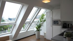 A modern kitchen with skylights, a large potted plant, and a view of the cityscape. - Kunsthaus Apartments (Vienna)