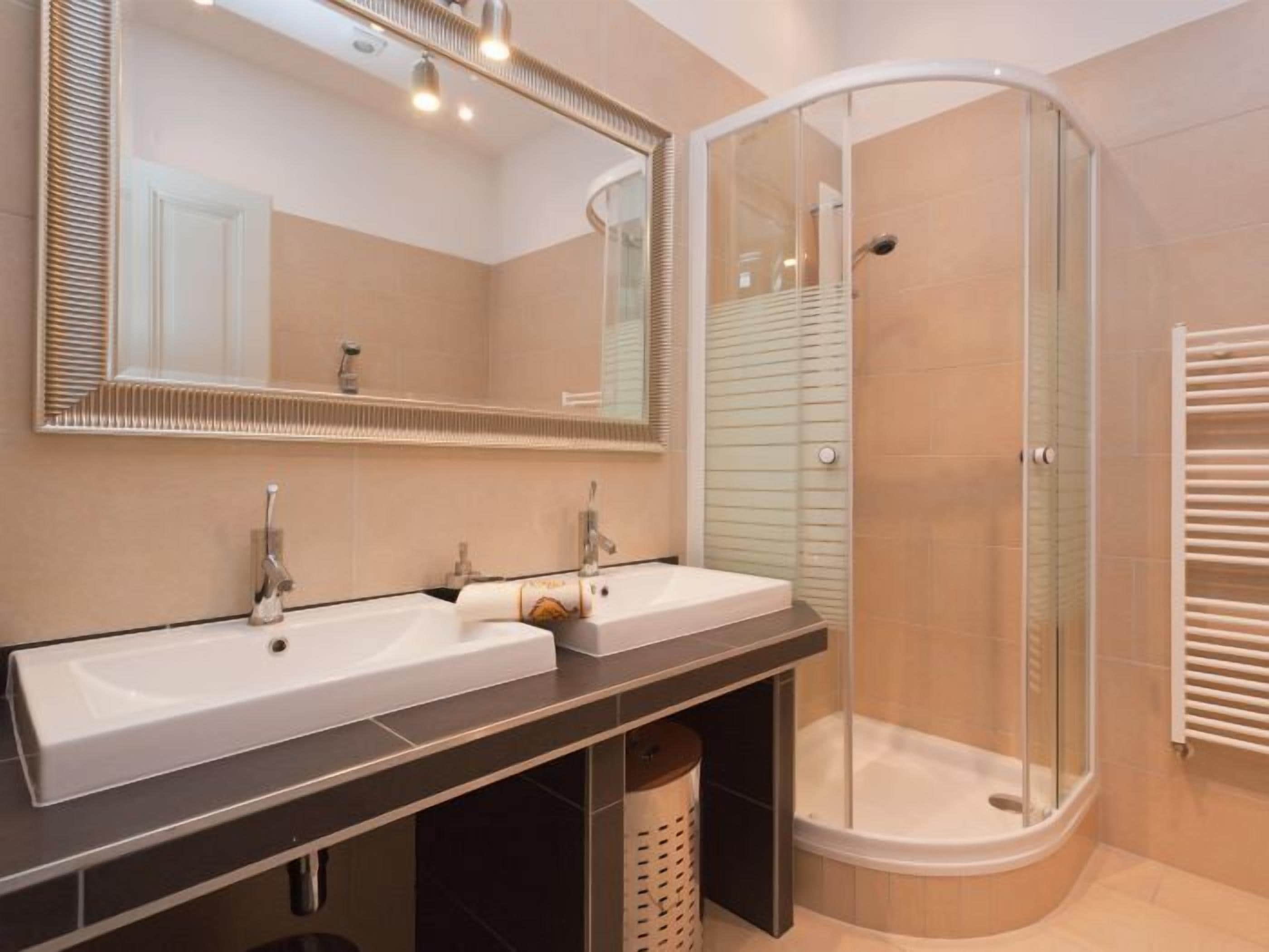 A modern bathroom with two sinks, a glass-enclosed shower, and a large mirror.