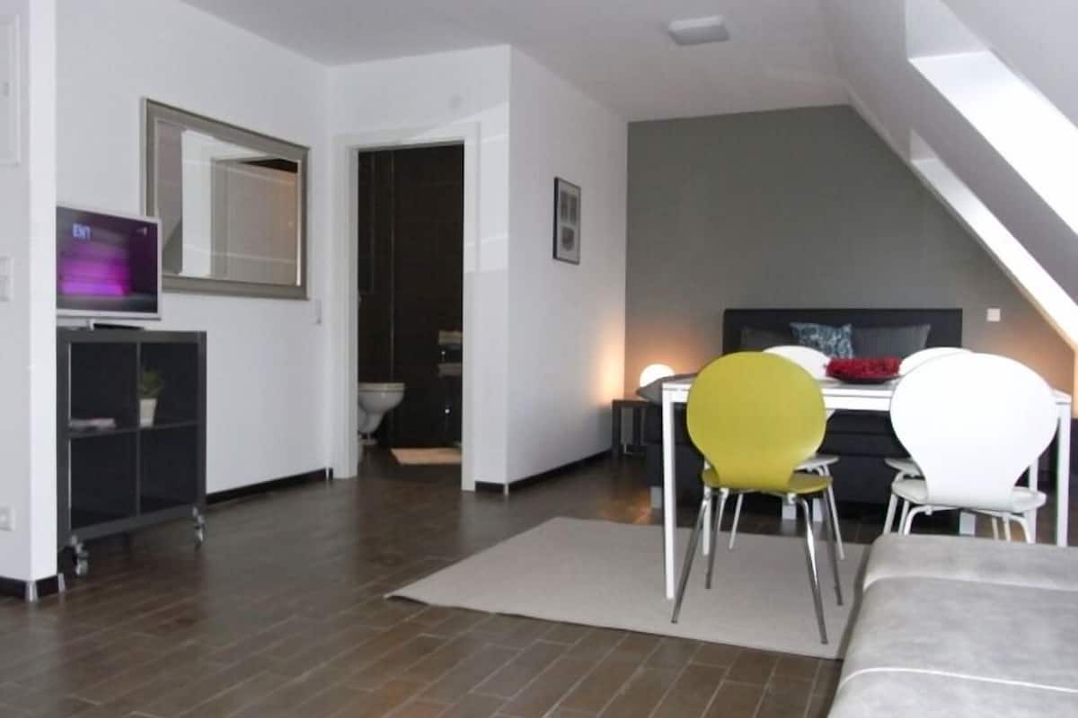 A modern living room with a dining area, a television, and a staircase.