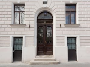 Un bâtiment à la façade symétrique, doté d’une entrée centrale en arc surmontée d’une porte en bois foncé, flanquée de deux portes plus petites.